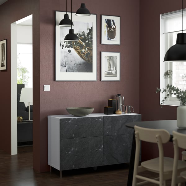 White BESTÅ sideboard with dark marble, holding decorative items. Tall, surrounded by light wood chairs.