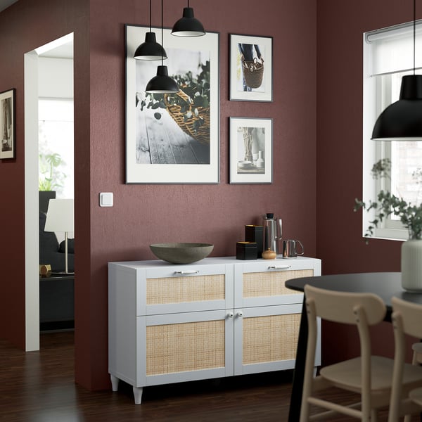 Stylish dining area with white and rattan sideboard, marble bowl, hanging lamps, and artwork. It is a prominent piece against burgundy wall.