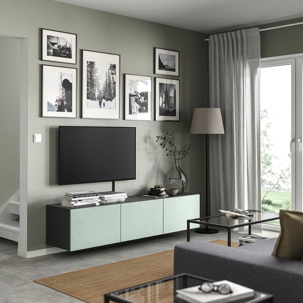 Modern living room with grey walls, light green BESTÅ tv unit, flat-screen tv, black coffee table, photo gallery, floor lamp, and sliding glass door.