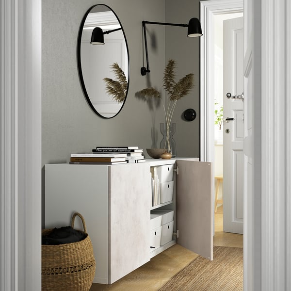 Minimalist entryway with BESTÅ cabinet, mirror, and wall lights. Open door reveals storage space.
