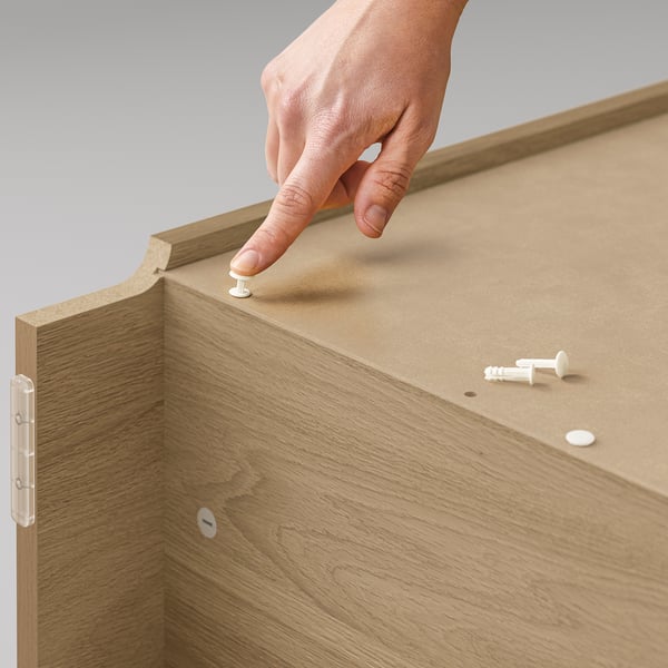 A person is assembling a BILLY light brown wooden bookshelf, using white connectors.