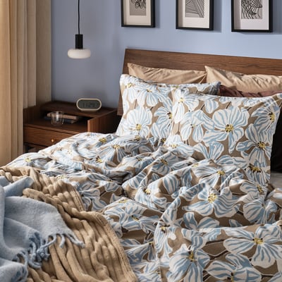 Bed with BÖNTRÄD blue/brown floral duvet, wooden headboard, lamp, clock, & blanket