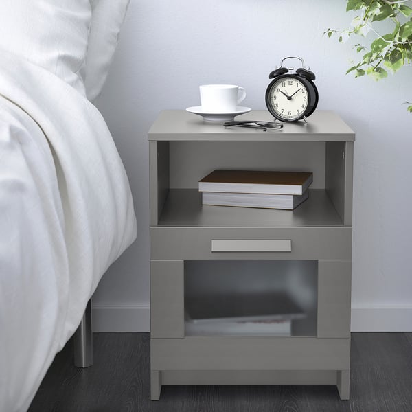 Minimalist bedroom with grey BRIMNES bedside table. Holds alarm clock, teacup, and books.