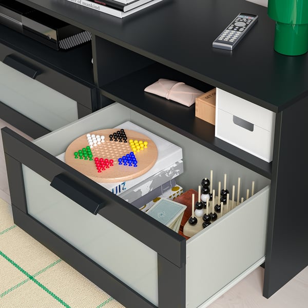 Open drawer of black BRIMNES tv storage, showing colourful game pieces.