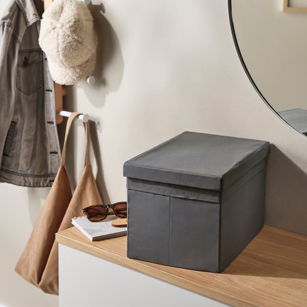 Grey storage box with lid on wooden shelf, layered with sunglasses, bag, and coat hook.