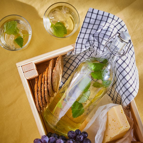 Wooden box with pitcher of elderflower drink, cheese, grapes, glasses, and cloth.