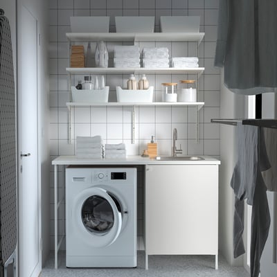 Modern white laundry setup. ENHET cabinet, sink, and washing machine. Neatly organised with shelves and accessories.