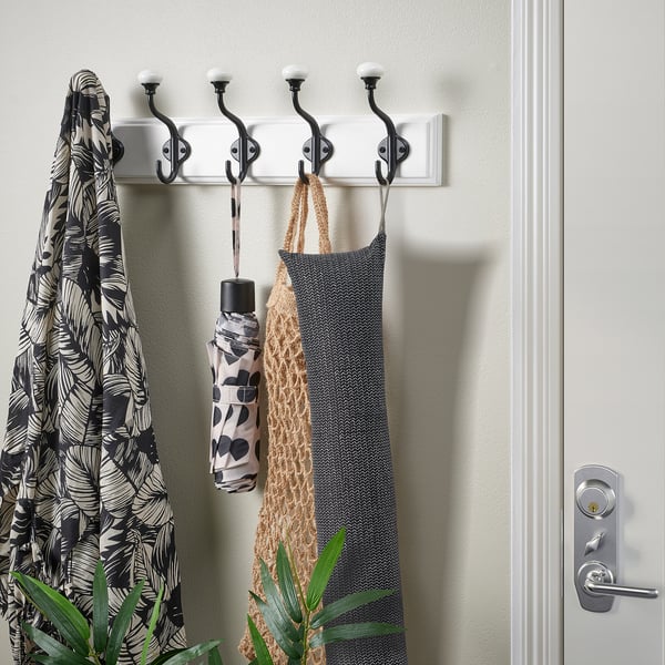 White coat rack with hooks holds scarf, umbrella, bag; next to door.