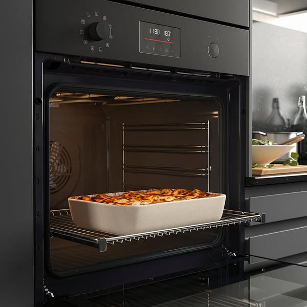 Black oven baking dish with golden-brown casserole, showcasing grill and fan cooking functions.
