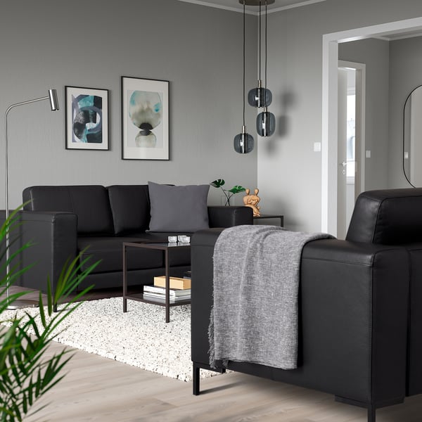 Modern living room with black sofa, grey cushions, throw, dark lights, abstract art, white rug, wooden floor.