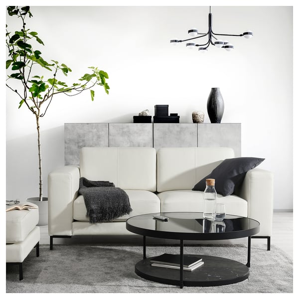 Modern living room with white leather FULLERÖ sofa, black coffee table, grey rug, and plant.