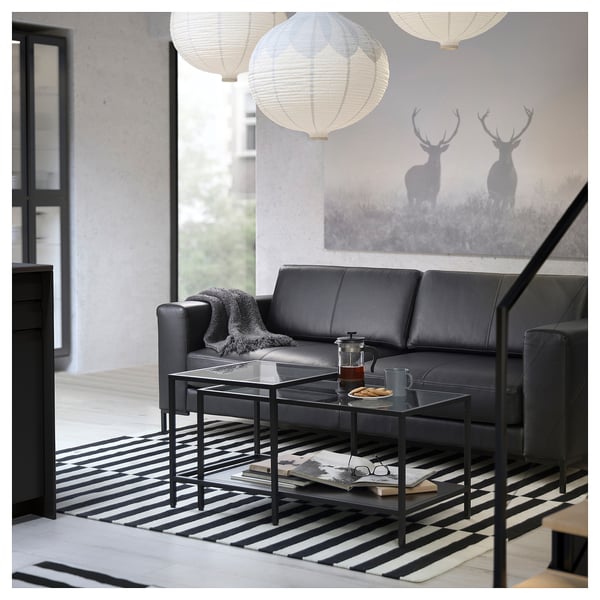 Modern living room with black FULLERÖ leather sofa, glass coffee table, striped rug, and hanging lanterns.
