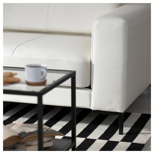 Modern living room with white leather sofa, striped rug, metal side table, mug, biscuits.