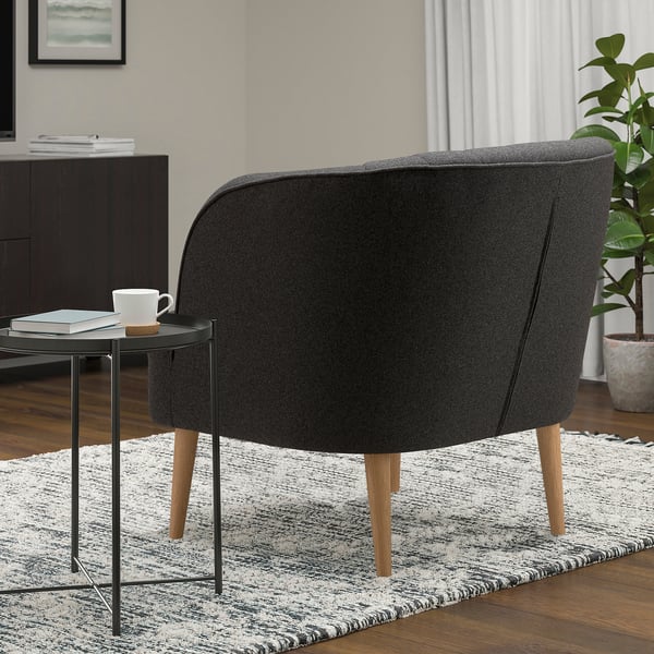 Black barrel chair with wooden legs on a striped rug beside a small table with a mug.