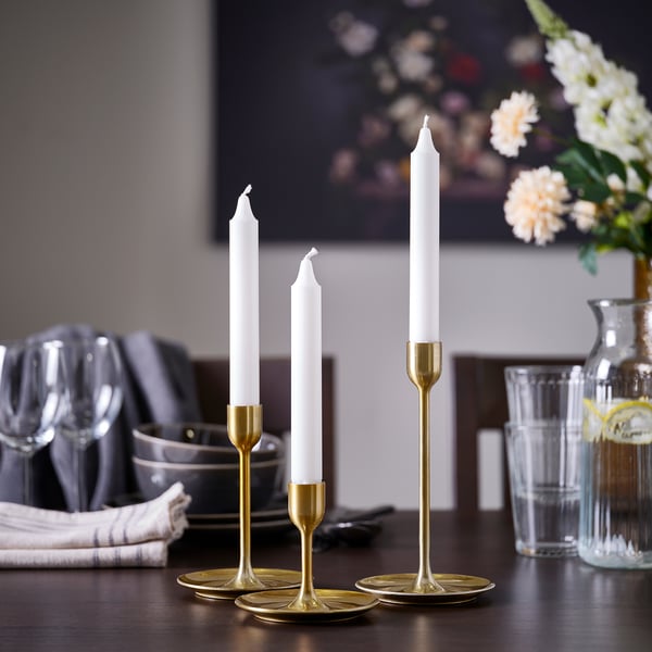 FULLTALIG: set of 3 brass candlesticks in varying heights, sleek modern design, placed on table near glasses and vase, creating cosy atmosphere.