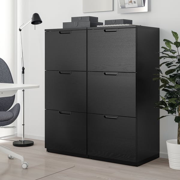 Black GALANT storage unit with 6 drawers, next to a grey chair and plant, offering closed storage.