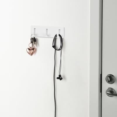 White wall holds keys and earphones with self-adhesive hooks.