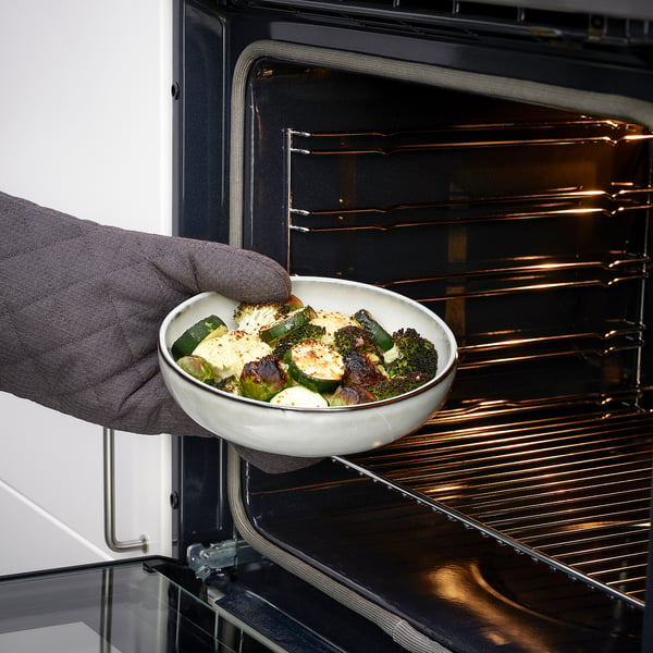 Person placing baked dish into oven. Product: GLADELIG oven dish.