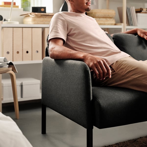 A person sits comfortably on a modern GLOSTAD sofa, showcasing its padded armrests and back cushions.