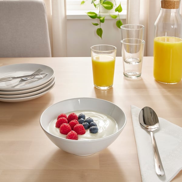 Table set with breakfast items: bowls of yoghurt with berries, juices, and plates with cutlery.