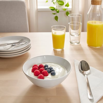 Table set with breakfast items: bowls of yoghurt with berries, juices, and plates with cutlery.