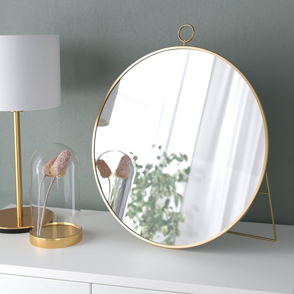 Round gold-framed mirror on stand; hangs or stands; reflective surface.