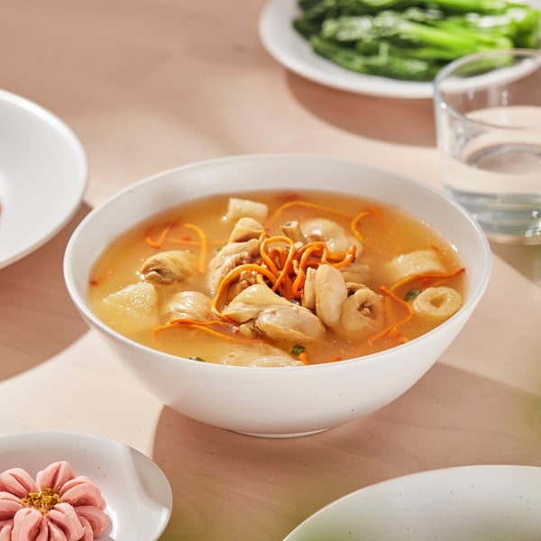Bowl of soup with noodles and vegetables on a table, surrounded by other dishes and a glass.