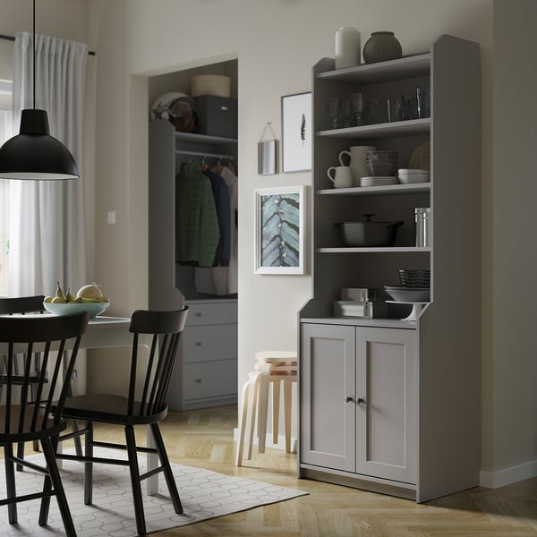 Modern dining room with HAUGA grey cabinet, black chairs, hanging light, and closet with clothes.