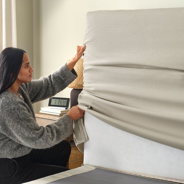 A person fitting a machine-washable mattress cover, suitable for HEMFJÄLLET divan bed.