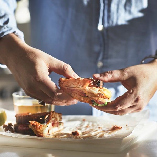 Hands holding a breakfast sandwich, showcasing even heat distribution and easy handling on all hobs.