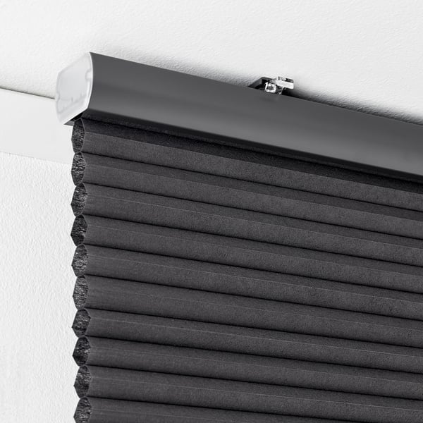 Black cellular blind mounted near the ceiling, showing the rolled-up portion and the hidden cord design for safety.
