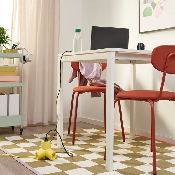 Small home office with white desk, red chair, laptop, water bottle. Yellow 4-way extension cord on floor.