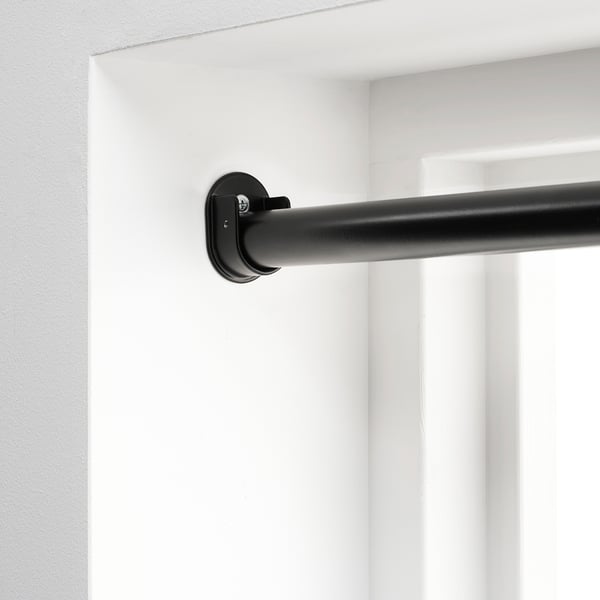 Black curtain rod bracket mounted on white wall, part of HUGAD system for hanging curtains between two opposite walls.