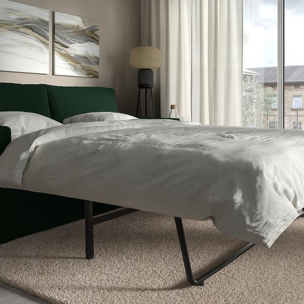 Modern bedroom with grey bedding, green headboard, and floor lamp. Window with city view.
