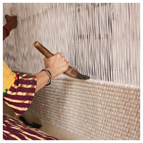 Person weaving on loom. Stripes on fabric. Hands gripping wood tool. Focused craftsmanship.