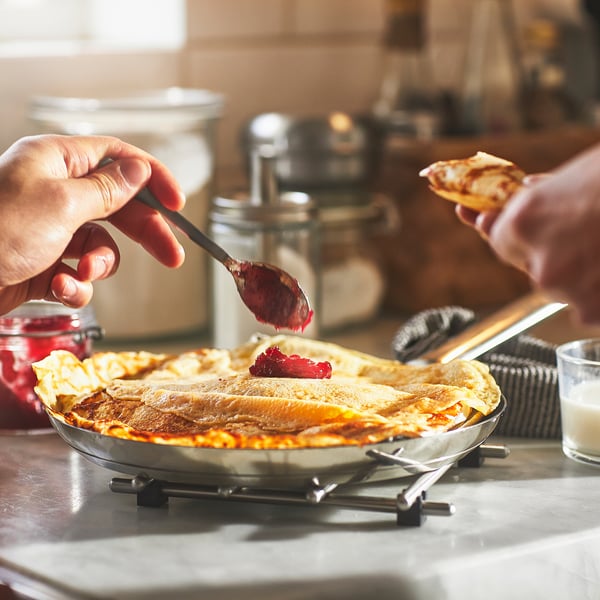 Person spreads jam on a pancake atop an IKEA 365+ pan on a stove. The pans non-stick surface ensures easy food handling.