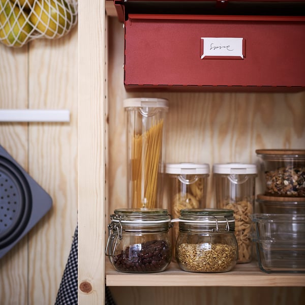 A well-organized kitchen shelf displaying glass jars with locking lids storing dry foods, including pasta, beans, and grains.