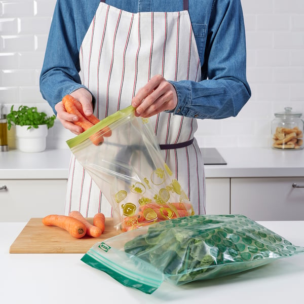 Person prepping vegetables with reusable sealable bags in kitchen.