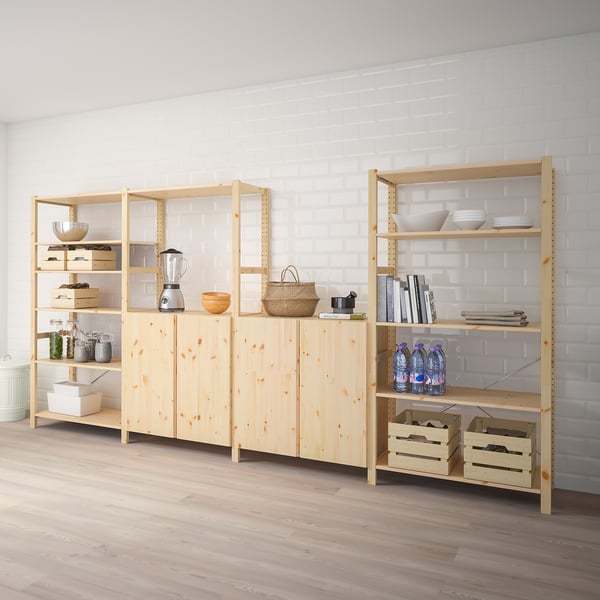 Wooden IVAR shelving units store kitchen items; blender, bowls, bottles, plates. Tall, light-colored, sturdy, and spacious.