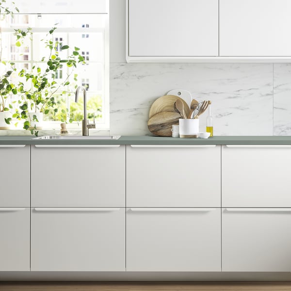 Bright kitchen with white JÄRSTORP counters & marble backsplash. Sink & greenery by window, tools on counter.