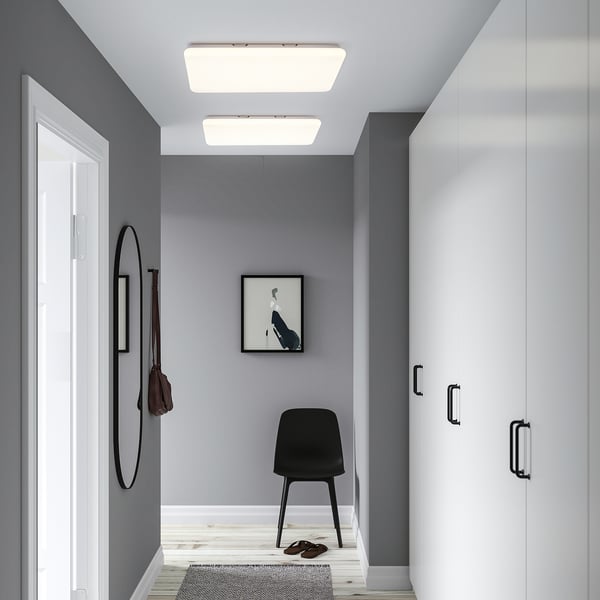 Modern hallway with grey walls, slim light panel, black chair, shoe rack, round mirror, and small rug.