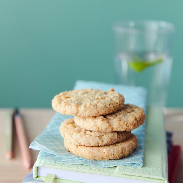 Stack of four oat cookies on blue napkin, glass, light green wall.
