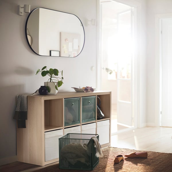 Modern entrance with KALLAX storage unit, featuring green bins, a mirror, and plants.