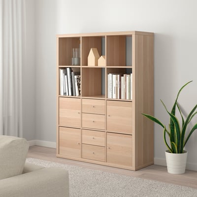KALLAX shelf unit with books, decor, and plant. Beige sofa partially visible.