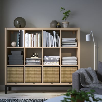KALLAX shelving unit with books, decor, plants & storage boxes, grey armchair partial.