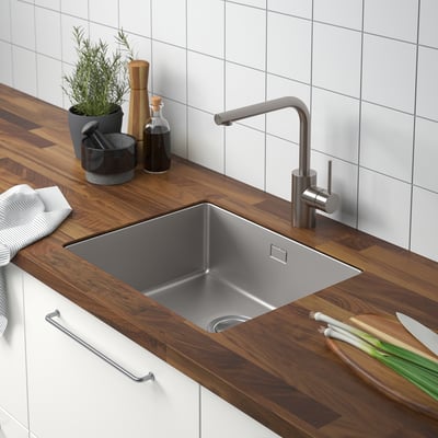 Wooden kitchen counter with stainless steel sink, modern tap, and accessories.