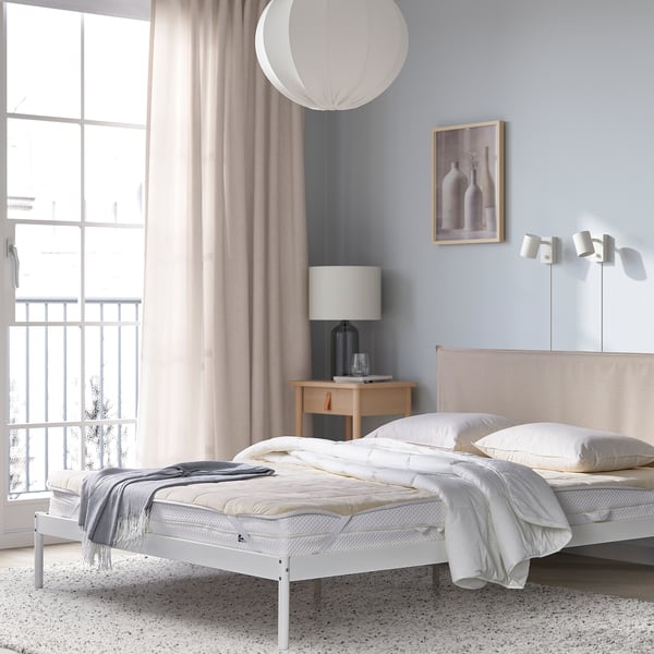 Cosy bedroom with white KEJSAROLVON mattress, light bedding, bedside table, lamp, large window, blue wall, artwork, pendant light.