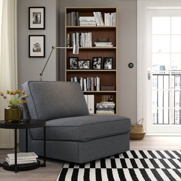 Modern grey KIVIK sofa-bed near bookcase, black & white rug, black side table with flowers, window.