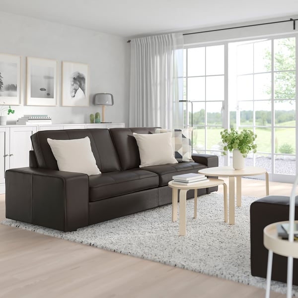 Modern living room with a spacious, dark grey KIVIK sofa, light pillows, wooden tables, and large windows.