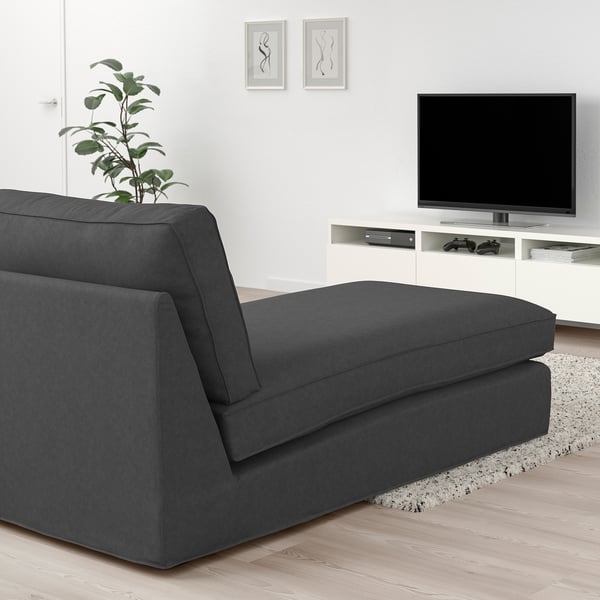 Modern living room with dark grey KIVIK sectional sofa, wooden floor, white tv stand, and wall art. Sofa appears large compared to other items.